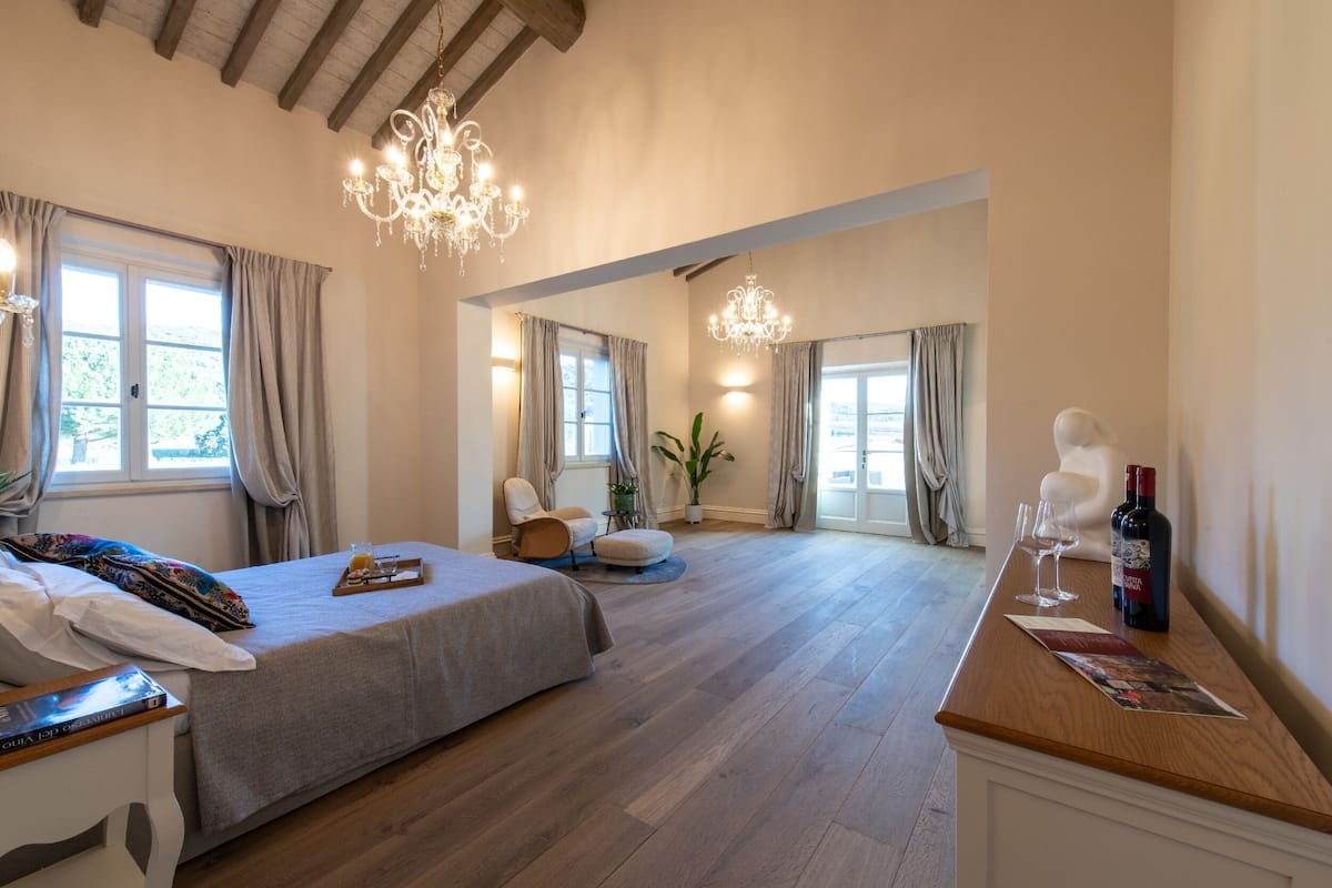 Ein geräumiges Schlafzimmer mit einem großen Bett, Holzboden, einer Chandelier und einem Essbereich mit Tisch und Stühlen.