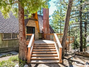 A wooden staircase leading to a cabin with a brick chimney, surrounded by trees. - Wolf Lodge in the Pines (Running Springs)