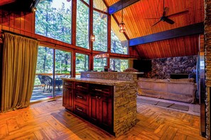 Una habitación amplia con ventanas grandes, una chimenea de piedra y un ventilador de techo de madera.