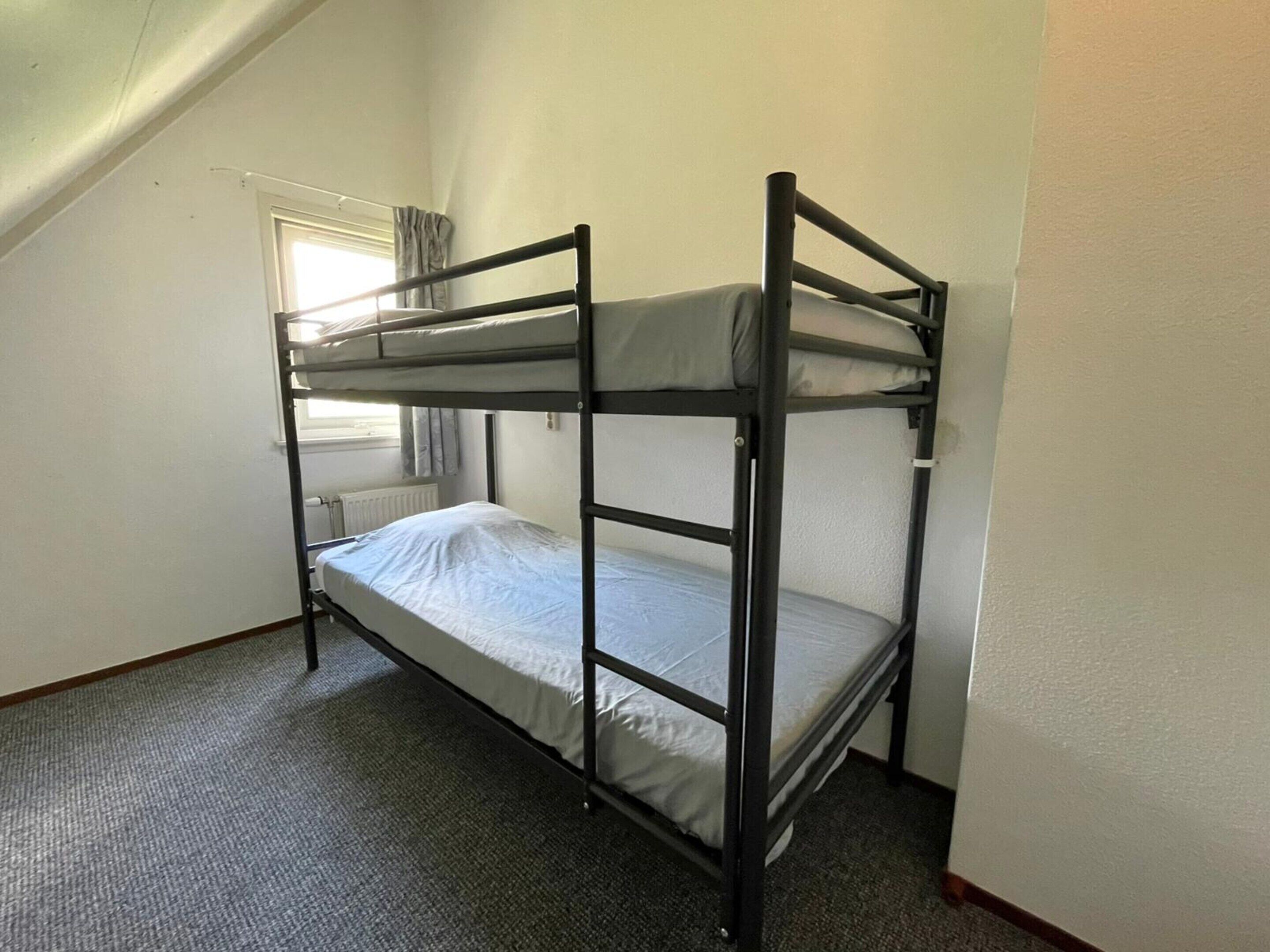 Een slaapkamer met stapelbed, raam, vloerbedekking en een radiator.