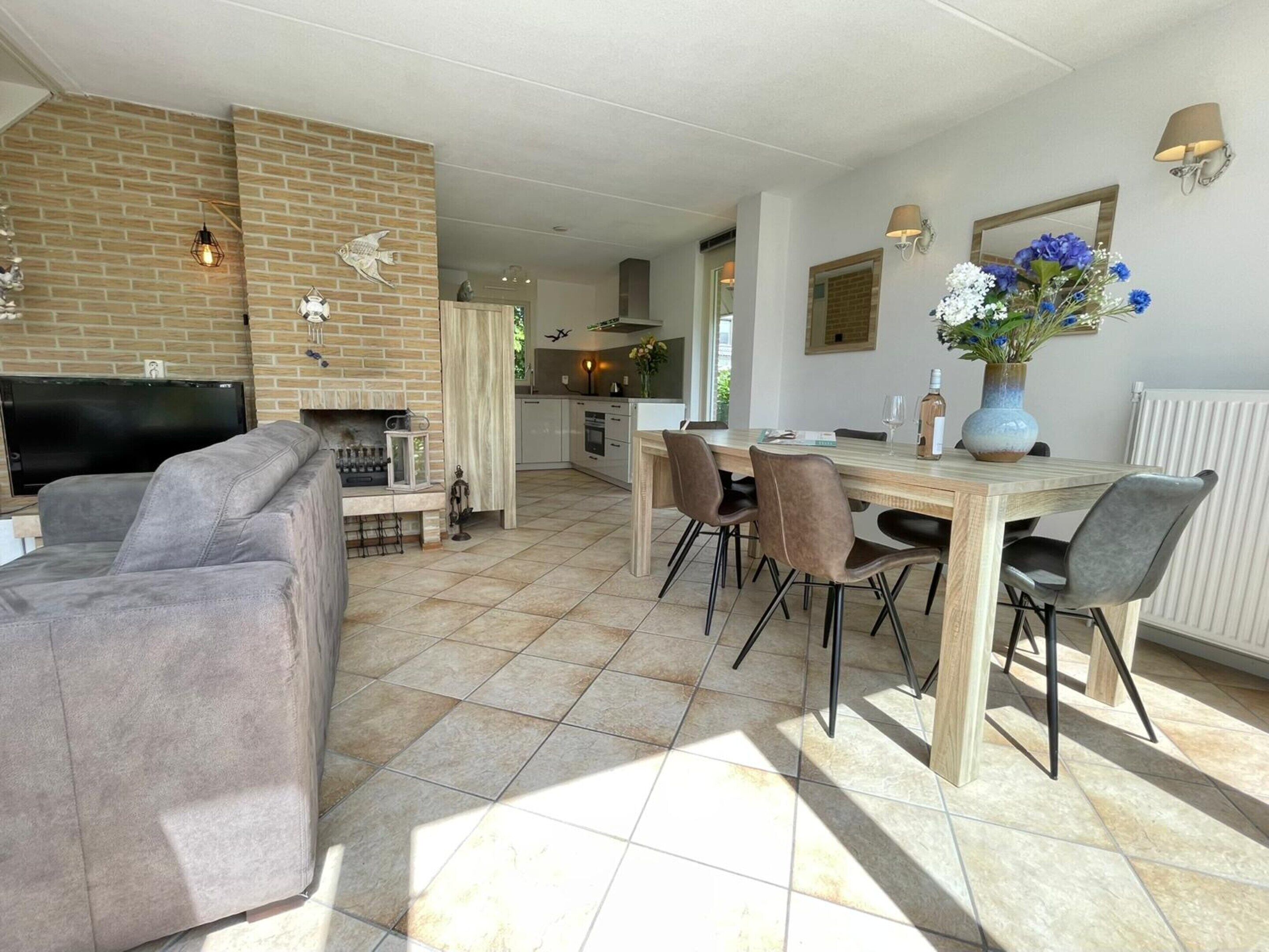 Un salon moderne avec une cheminée, un coin repas avec des chaises, une cuisine à l’arrière-plan et un téléviseur.