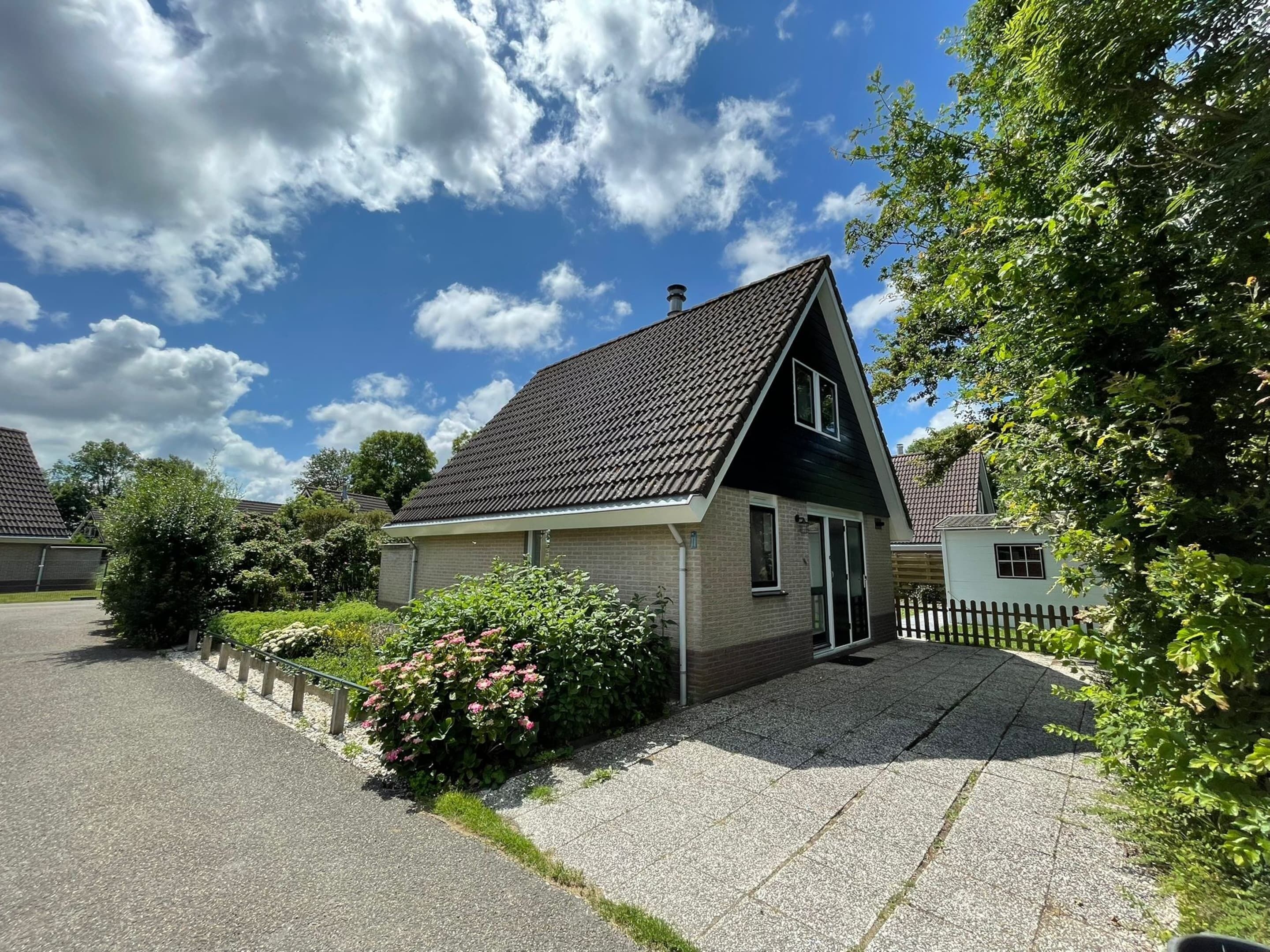 Ett bostadshus med ett sluttande tak, en ytterdörr och en liten trädgård med rosa blommor.