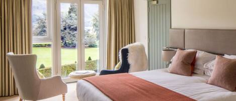 A hotel room with a large bed, a chair, a small table, and a view of a garden through a glass door.