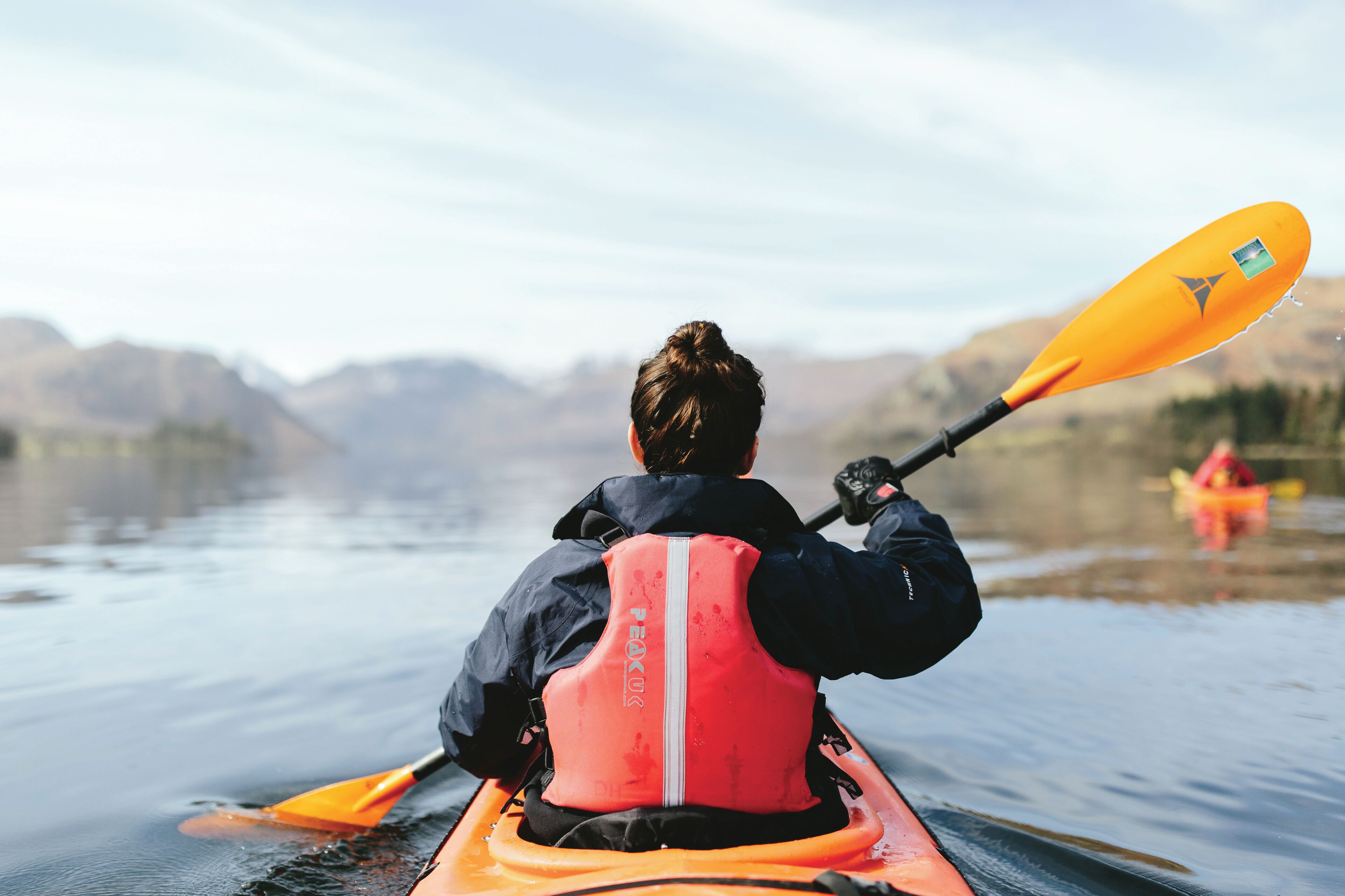 A person kayaking on a calm body of water with mountains in the background.