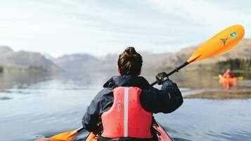 A person kayaking on a calm body of water with mountains in the background.