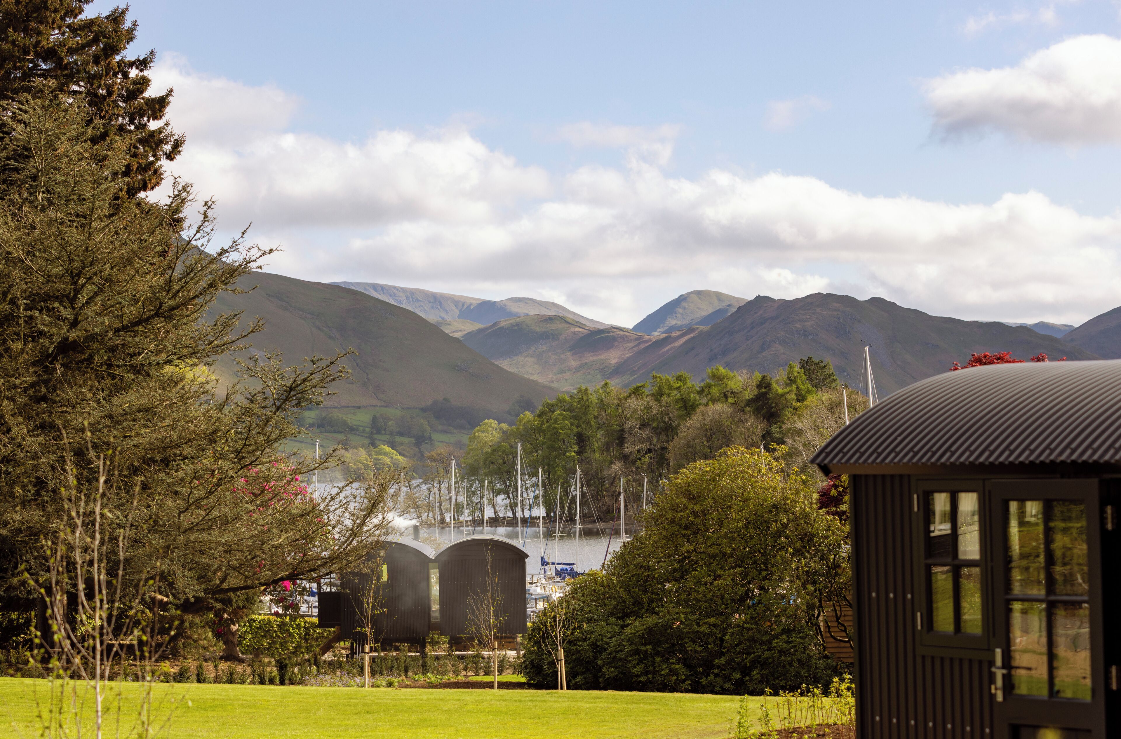 A rural landscape with mountains, a small building, and a body of water with boats.