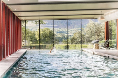 An indoor swimming pool with a view of a forested landscape through large windows.