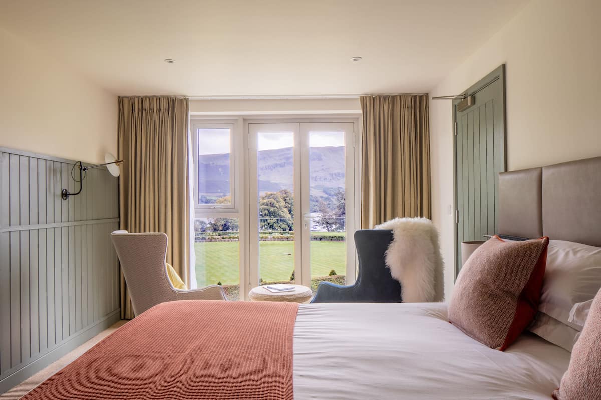 Habitación de hotel con cama, una silla, vistas al exterior y una ventana con cortinas.