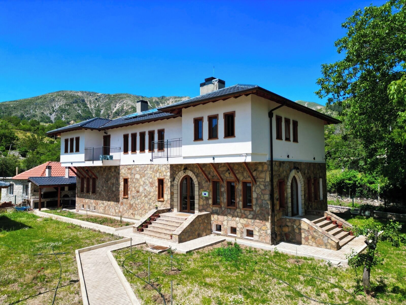 A two-story house with stone and plaster walls, a balcony, and a staircase leading to the upper floor.