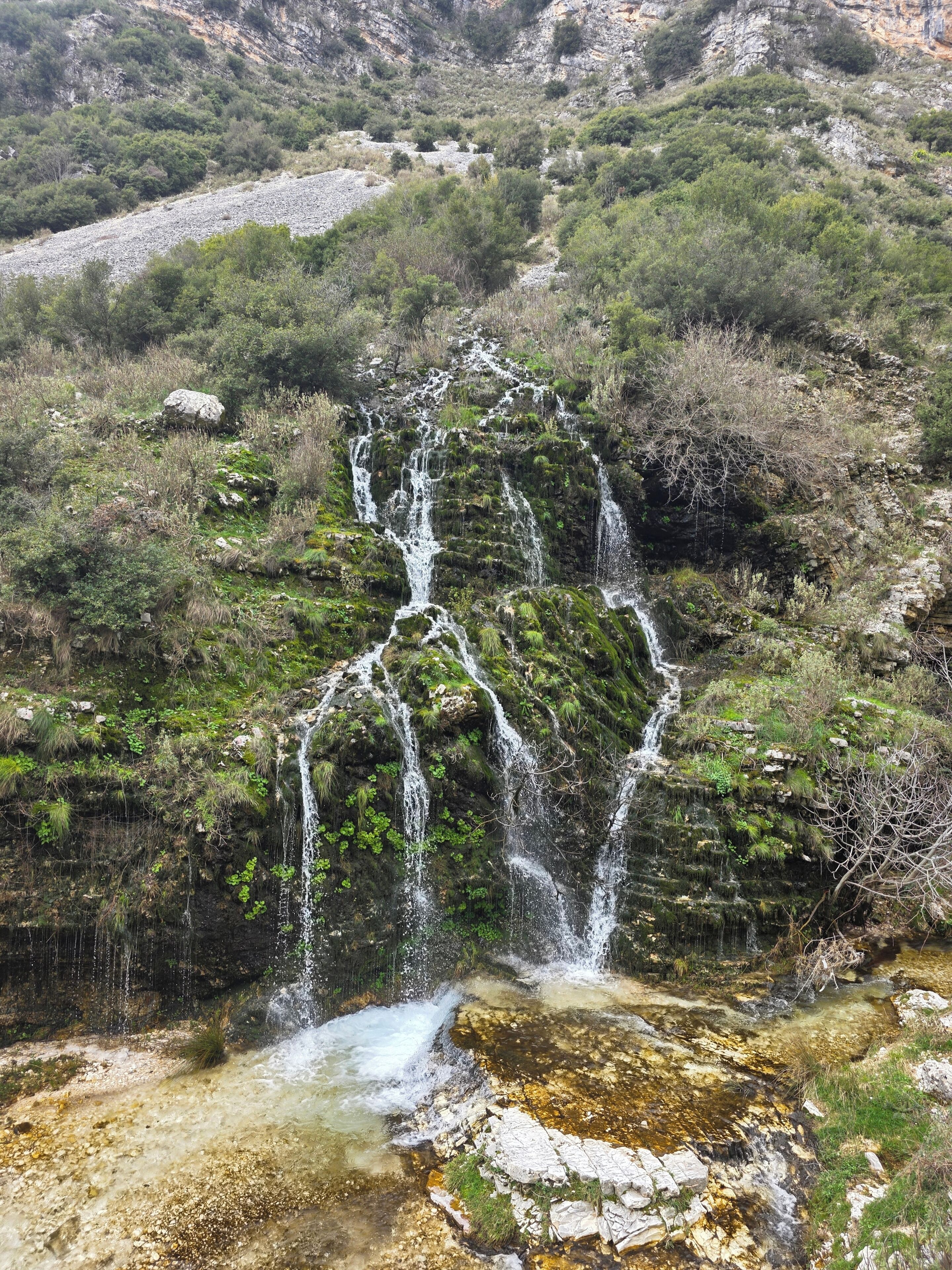 Una cascada que es precipita per un penya-segada rocosa, envoltada de vegetació.