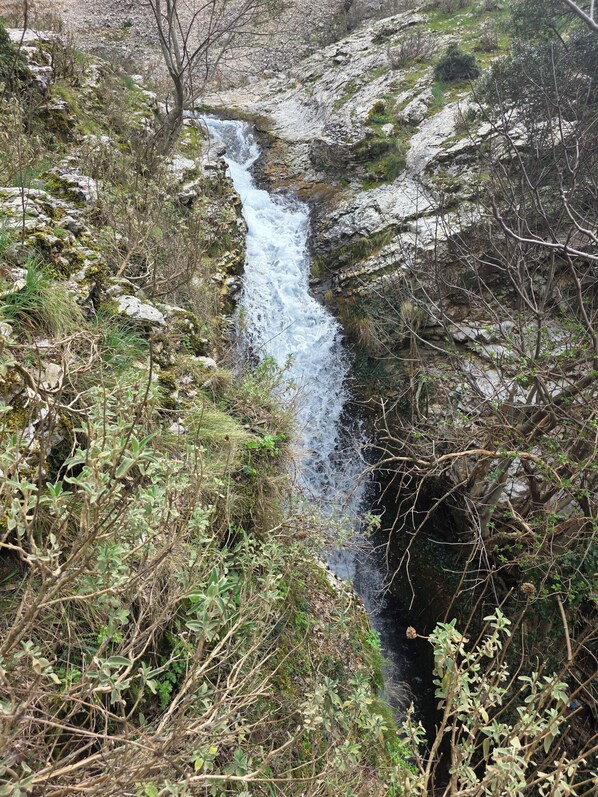 A natural waterfall surrounded by rocky terrain and sparse vegetation.