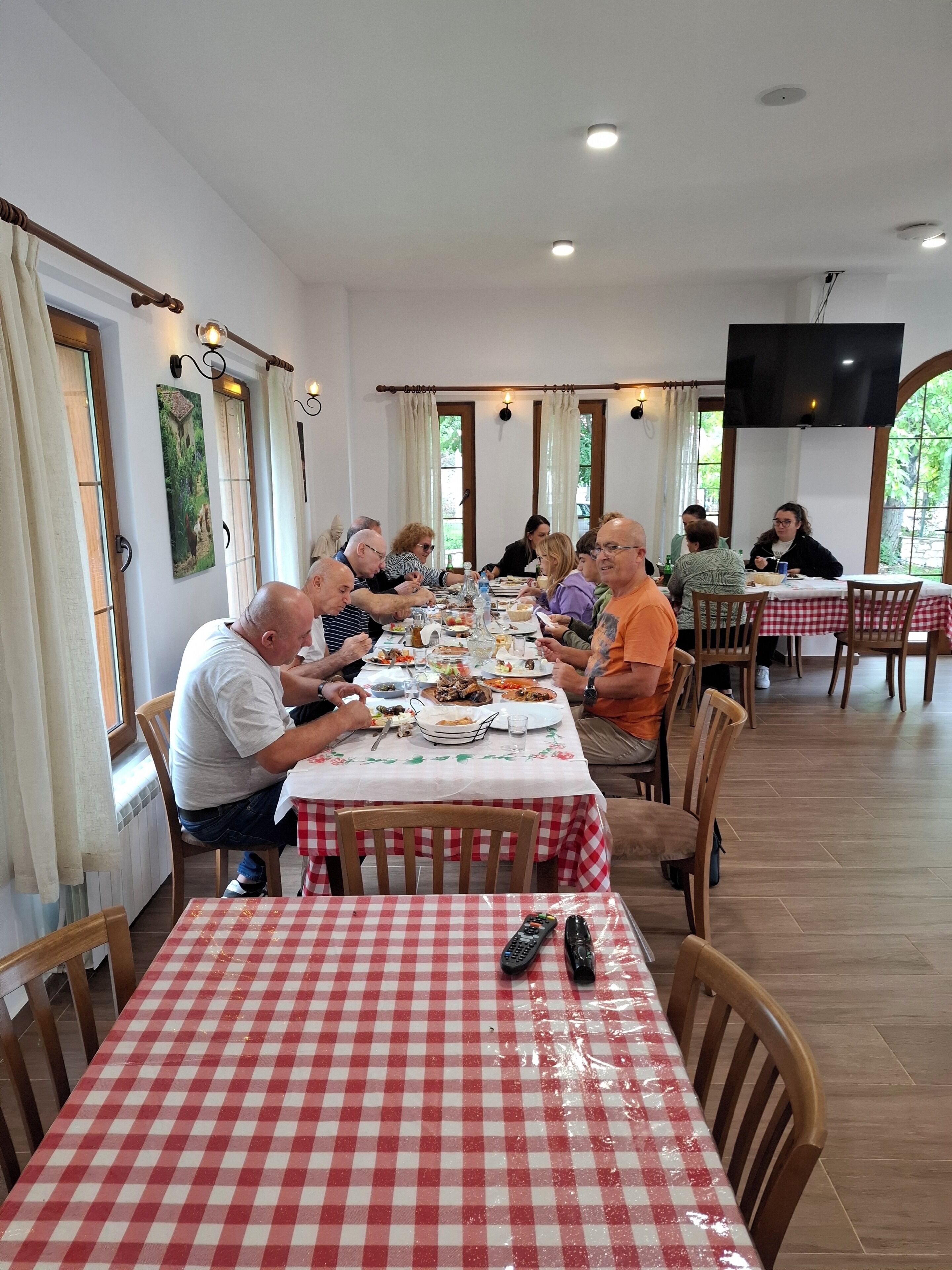 Zona pranzo con un tavolo lungo, sedie e una televisione montata a parete.