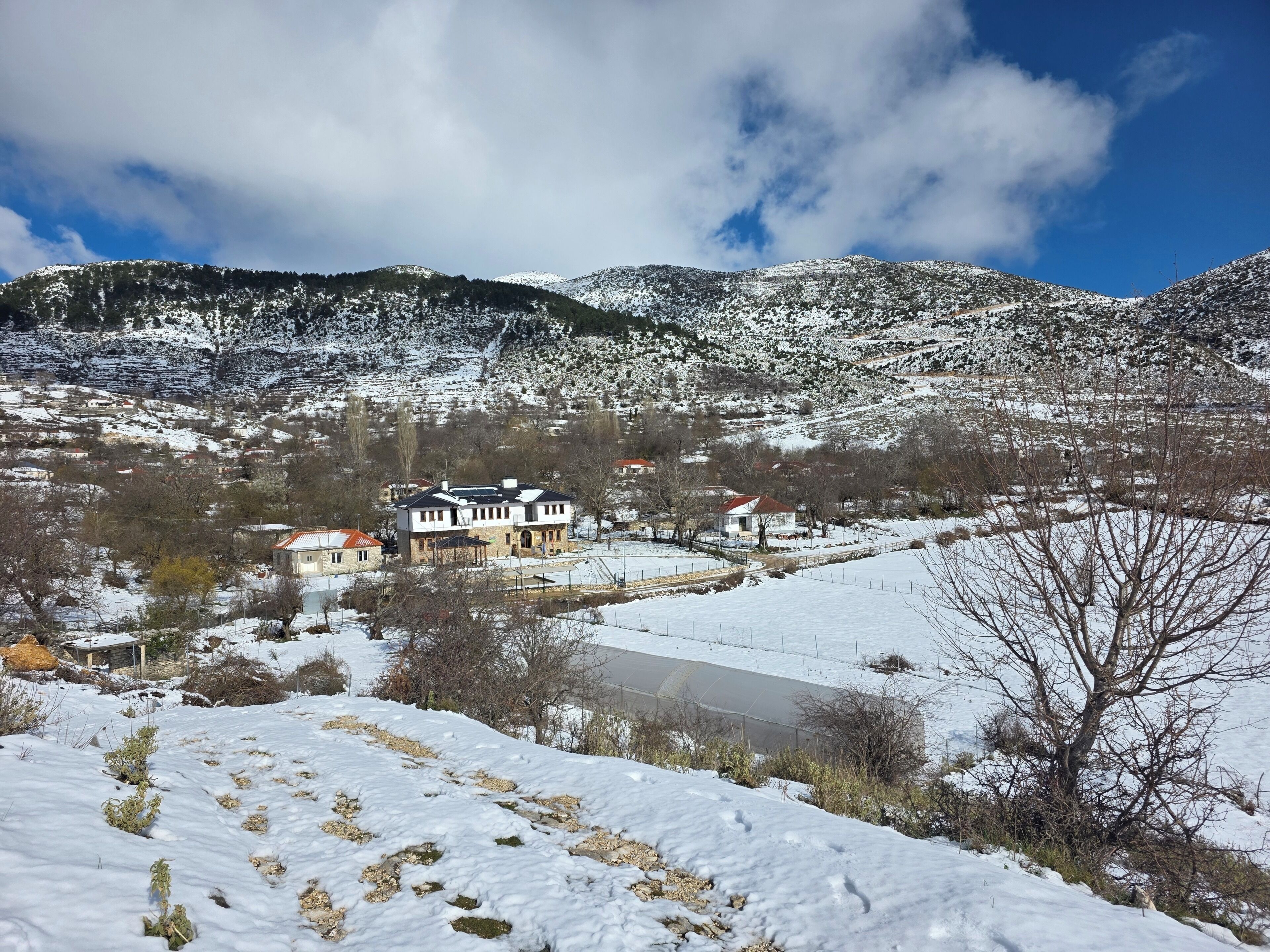 A snow-covered landscape with a house and a body of water.