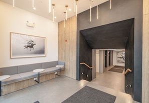 A modern lobby with a bench seating area, a framed artwork, and a staircase leading to another level. - 2-bedroom condo with king beds in Kelowna across from Gyro Beach. Rooftop Deck. (kelowna)