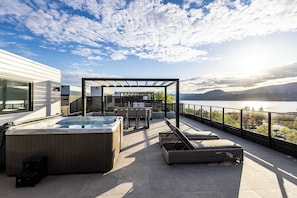 Une terrasse sur le toit dotée d’un jacuzzi, de chaises longues et d’une pergola offrant une vue sur un lac.