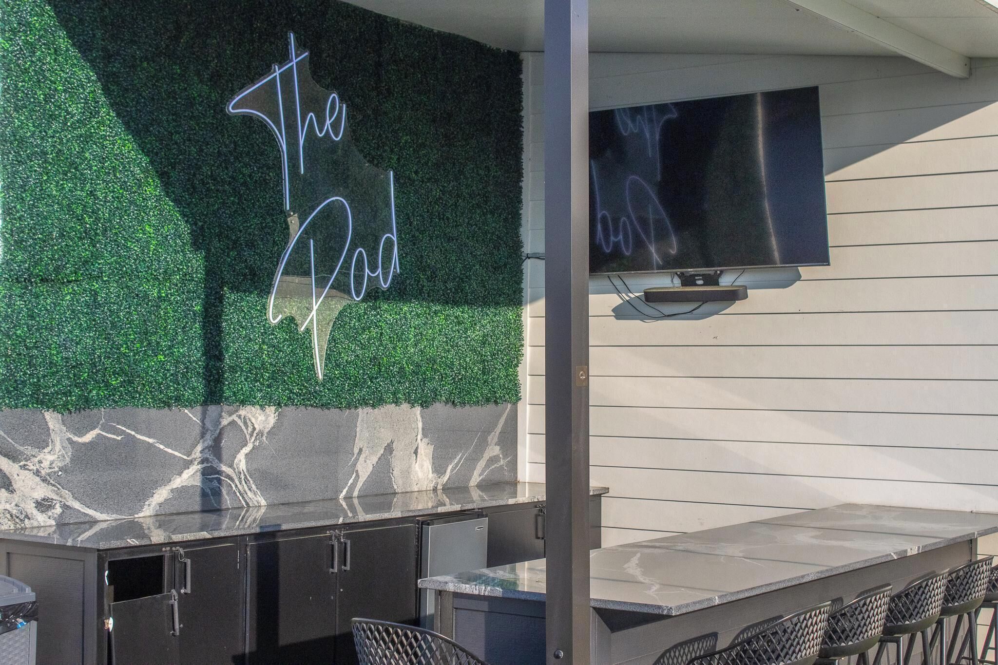 Zona de bar al aire libre con un letrero de neón, un televisor de pantalla plana y una encimera de mármol.