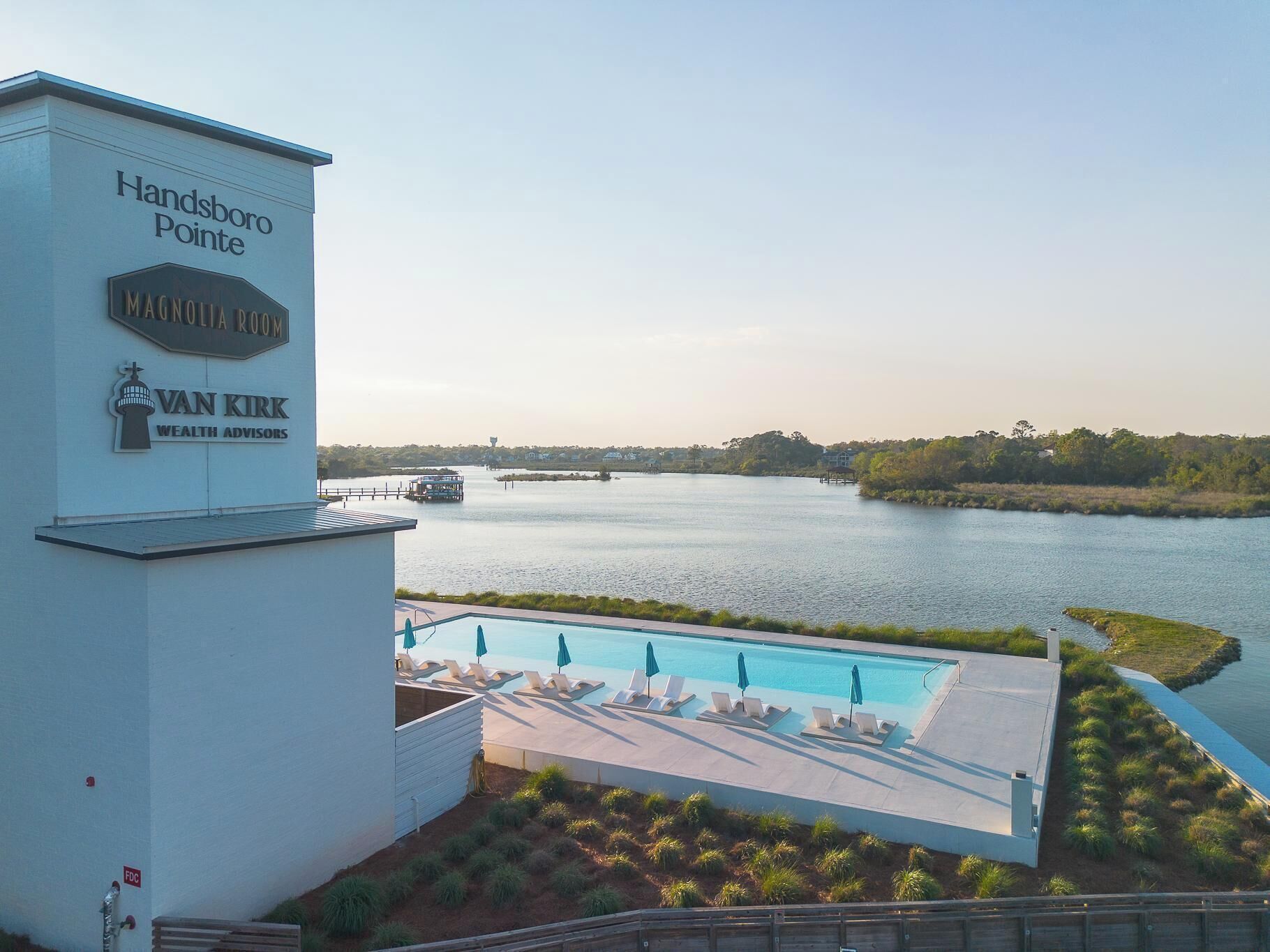 A waterfront hotel with a pool area, lounge chairs, and a view of the river.