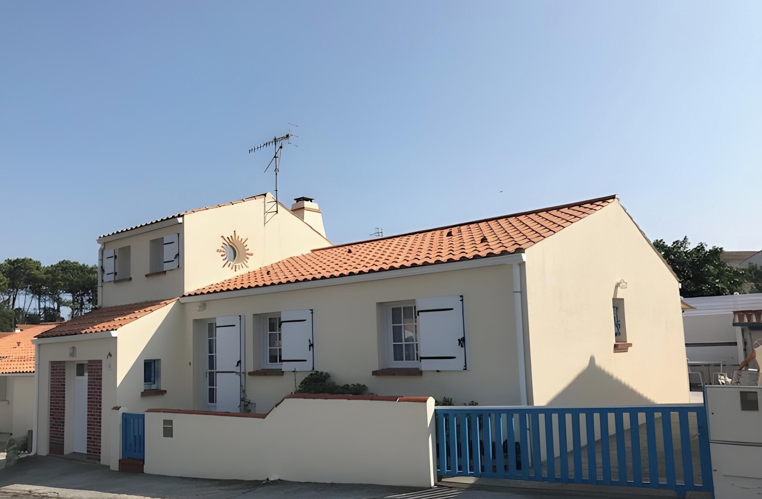 A two-story building with a tiled roof, a blue gate, and a sun dial on the facade.