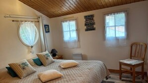 A bedroom with a bed, pillows, a chair, and a wall sign. - Maison Malovyn: Quiet House Near Beach and Forest (La Tranche-sur-Mer)