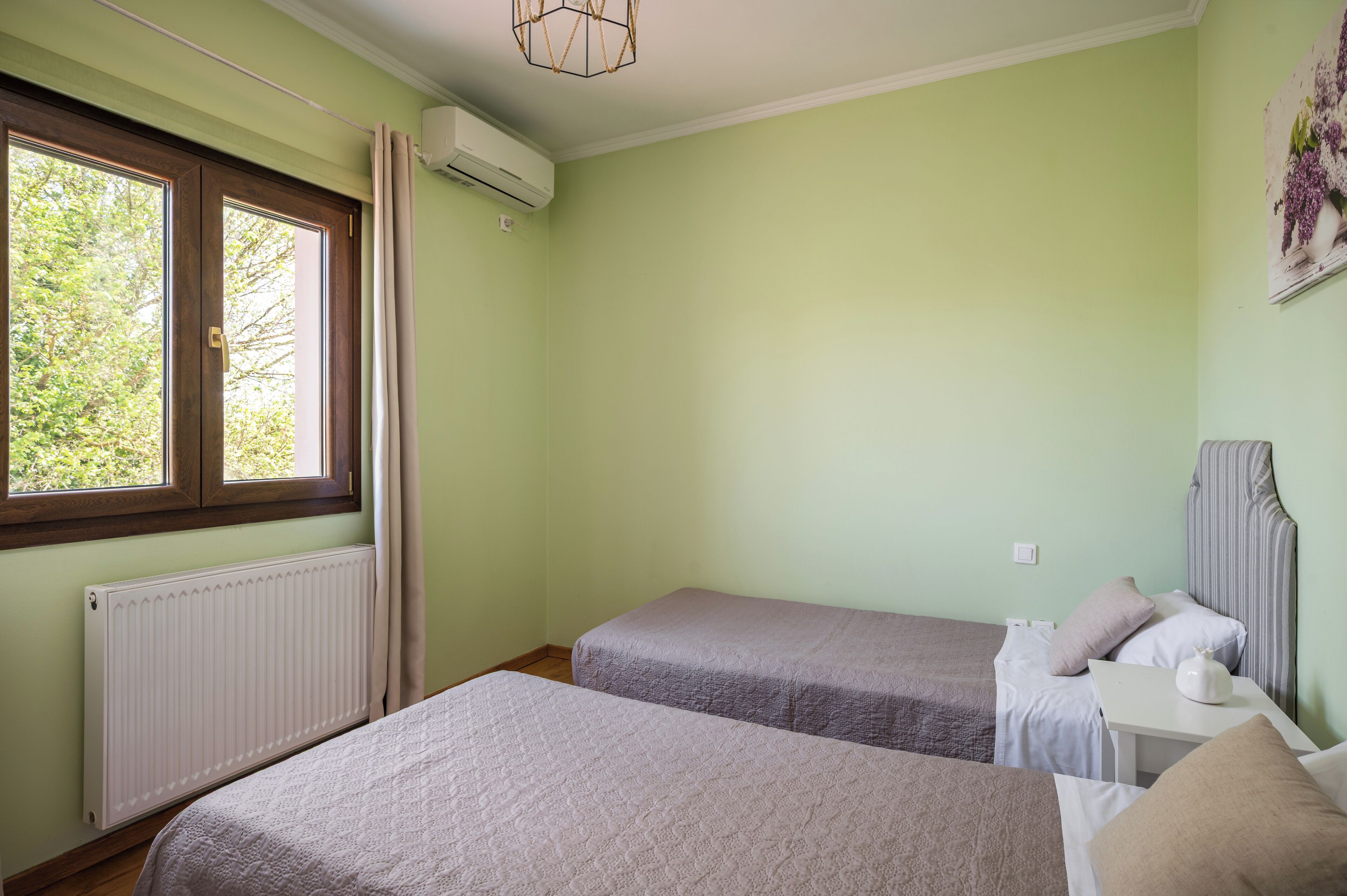 Une chambre avec deux lits, un radiateur, un appareil de climatisation, une fenêtre avec des rideaux et un luminaire fixé au mur.