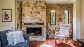 Una chimenea de piedra, una silla de madera, un sofá y un cuadro enmarcado en la pared.