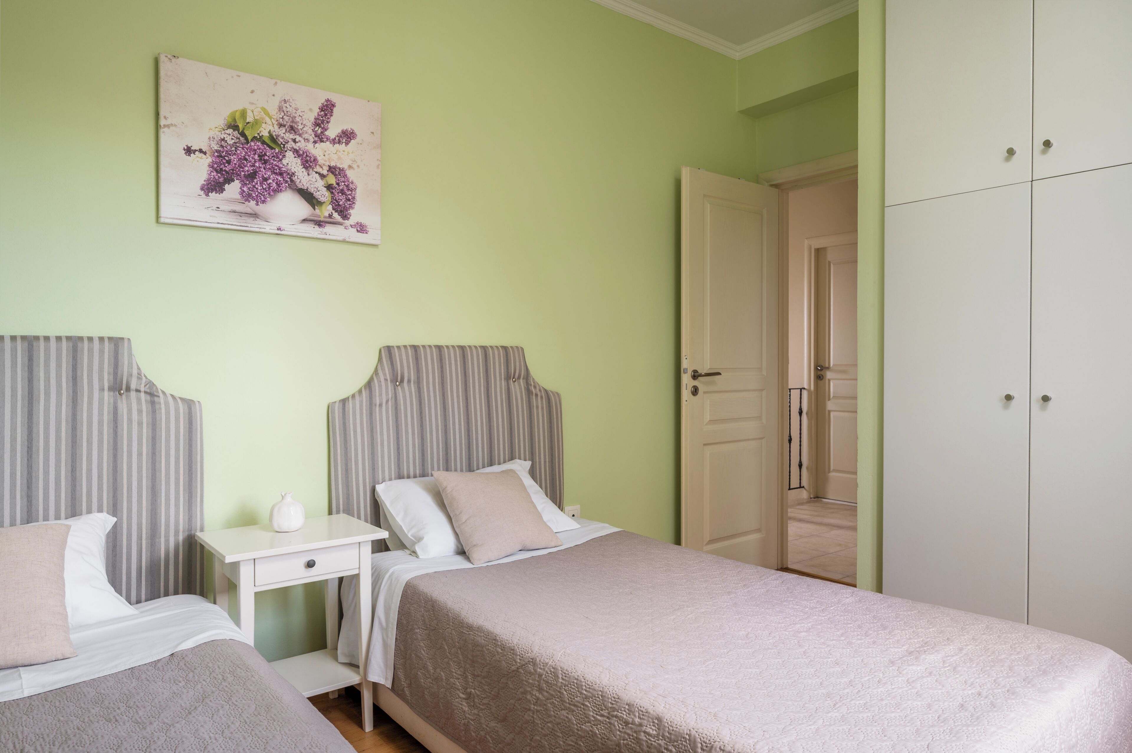 A bedroom with two beds, a nightstand, a dresser, and a door leading to another room.