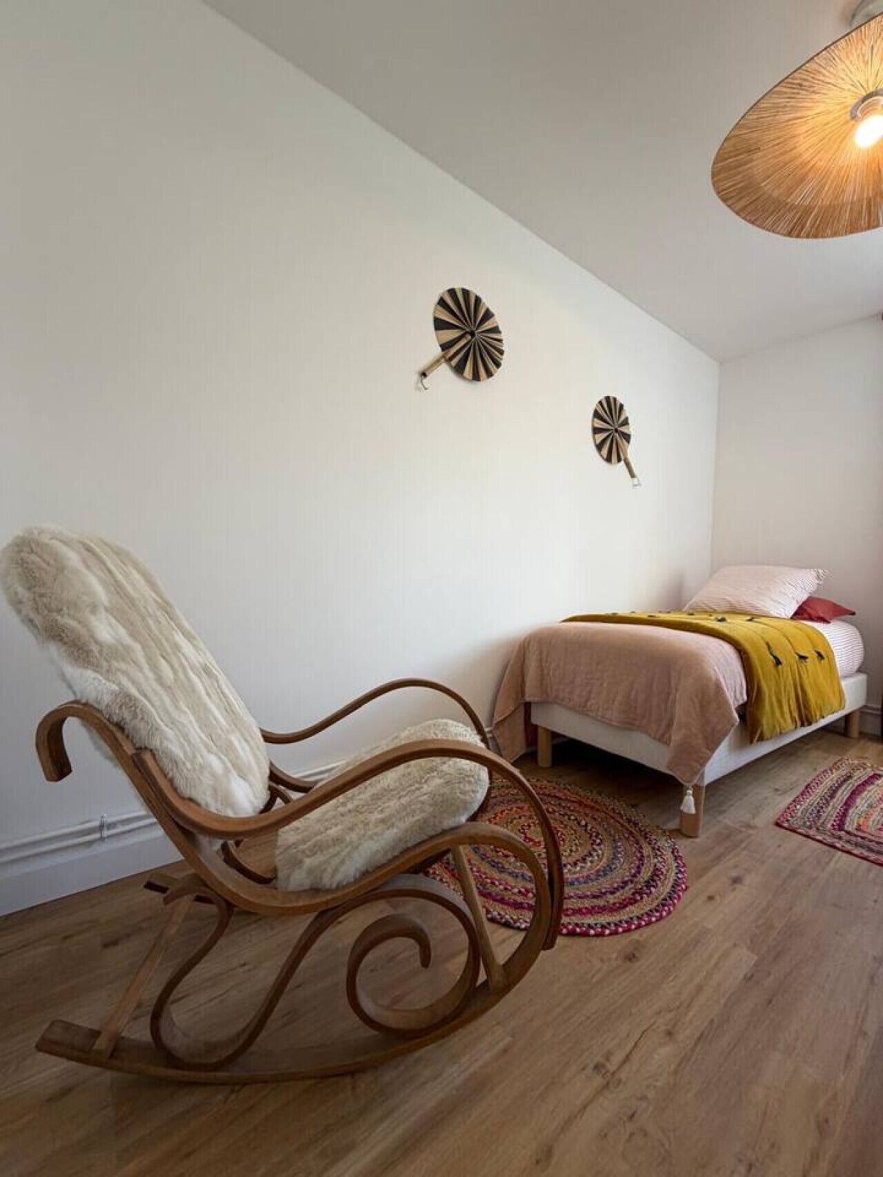 Un dormitorio con una mecedora de madera, una cama con una manta amarilla y dos adornos en la pared.