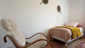 Un dormitorio con una mecedora de madera, una cama con una manta amarilla y dos adornos en la pared.
