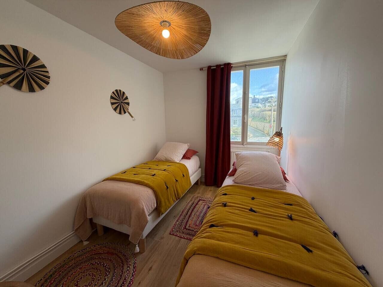Ein Schlafzimmer mit zwei Betten, einem Fenster mit Vorhängen, einem Deckenventilator und Wanddekorationen.