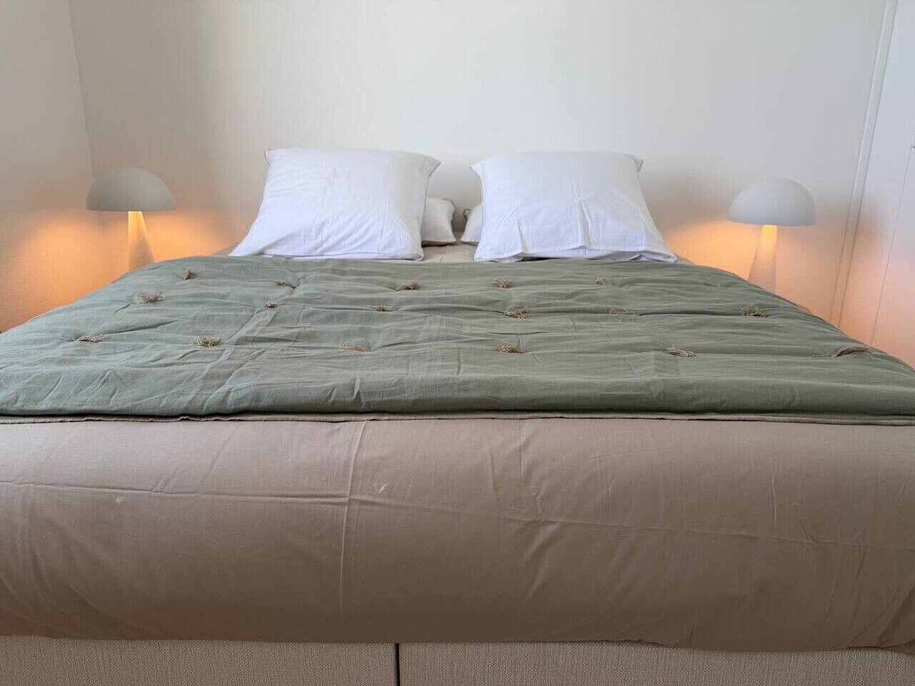 A bed with a green quilt and two white pillows, flanked by two bedside lamps.