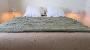 A bed with a green quilt and two white pillows, flanked by two bedside lamps.