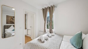 Un dormitorio con cama, espejo, ventana con cortinas y vistas al exterior.