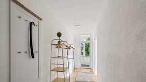 Un pasillo estrecho con una puerta blanca, una escalera de madera y una pequeña planta en maceta.