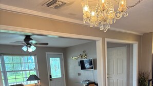 A dining area with a glass-top table, wooden chairs, and a chandelier. - Relaxing Punta Gorda Getaway 3BR, Kayaks, Outdoor Oasis (Punta Gorda)