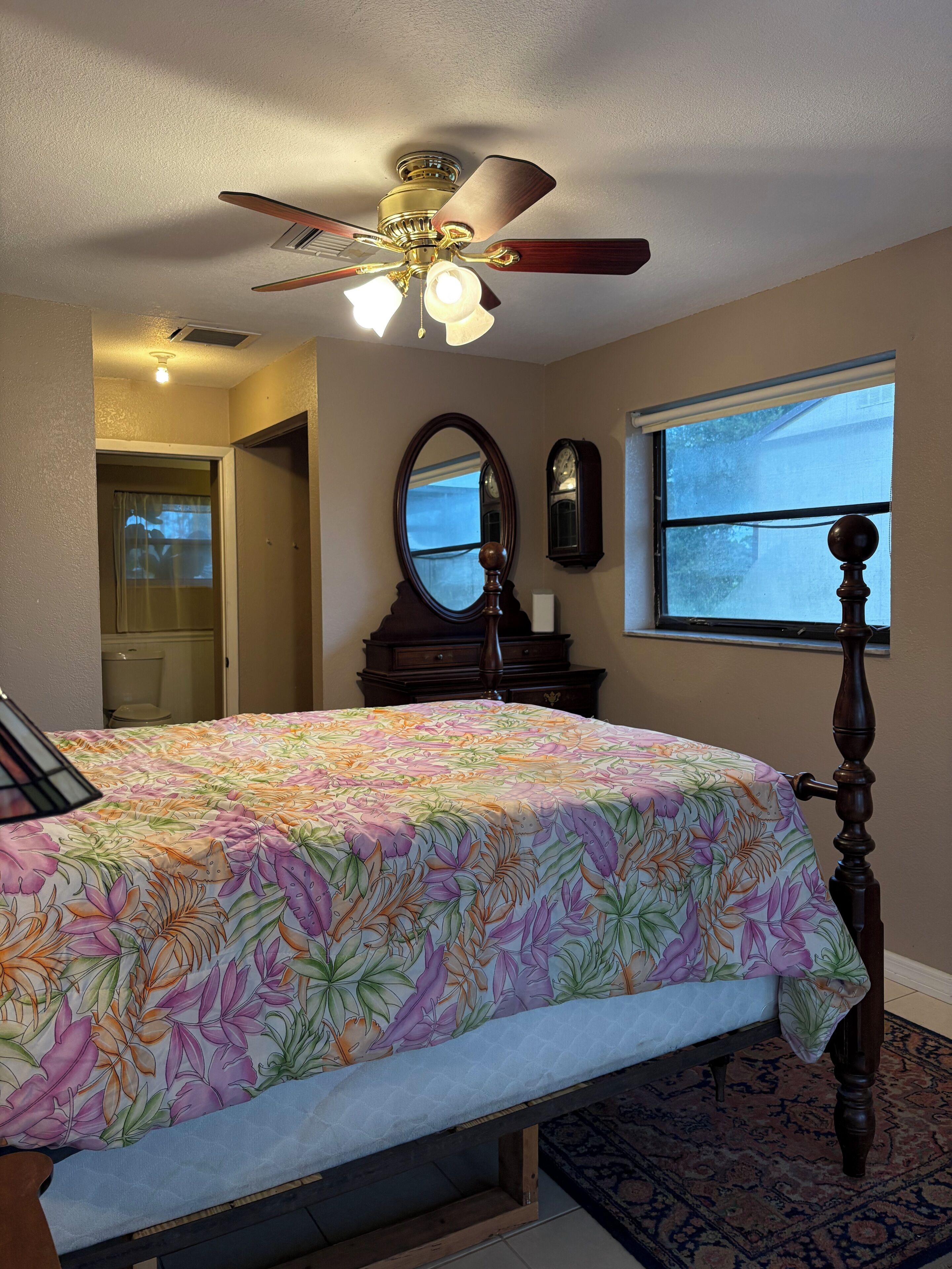 A bedroom with a bed, a ceiling fan, a window, a mirror, and a dresser.