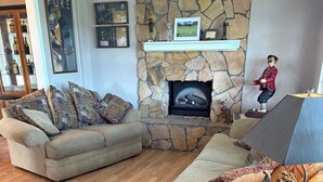 A living room with a stone fireplace, a sofa, a coffee table with a framed picture, and a wooden floor. - Relaxing Punta Gorda Getaway 3BR, Kayaks, Outdoor Oasis (Punta Gorda)