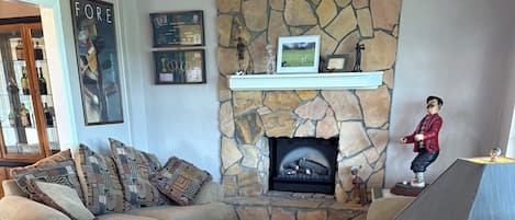 A living room with a stone fireplace, a sofa, a coffee table with a framed picture, and a wooden floor.