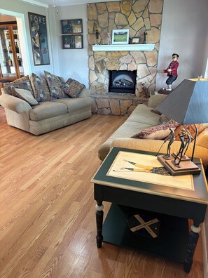 A living room with a stone fireplace, a sofa, a coffee table with a framed picture, and a wooden floor. - Relaxing Punta Gorda Getaway 3BR, Kayaks, Outdoor Oasis (Punta Gorda)