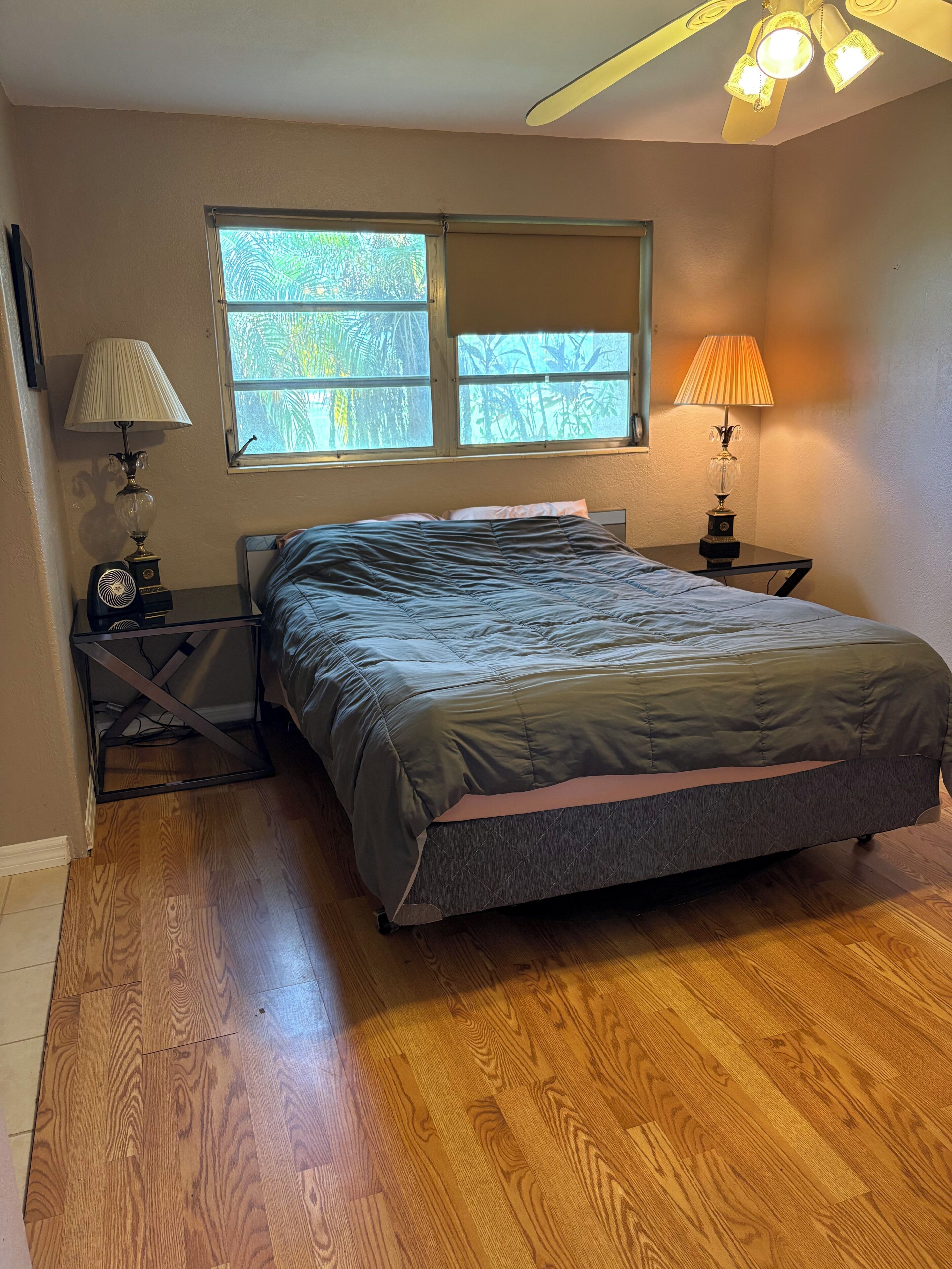 A bedroom with a bed, two bedside tables, a window, and a ceiling fan.