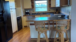 A kitchen with wooden cabinets, a black refrigerator, a window with a view, and a bar stool. - Relaxing Punta Gorda Getaway 3BR, Kayaks, Outdoor Oasis (Punta Gorda)
