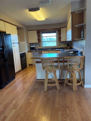 A kitchen with wooden cabinets, a black refrigerator, a window with a view, and a bar stool. - Relaxing Punta Gorda Getaway 3BR, Kayaks, Outdoor Oasis (Punta Gorda)