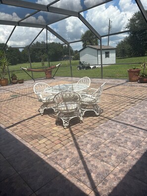 A covered patio with a table and chairs, potted plants, and a view of a house and lawn. - Relaxing Punta Gorda Getaway 3BR, Kayaks, Outdoor Oasis (Punta Gorda)