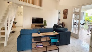 Uma sala de estar ampla com pé direito alto, uma escada, um sofá azul grande, uma mesa de centro de madeira e uma televisão.