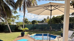 Um deck de madeira com piscina, espreguiçadeiras e um guarda-sol.