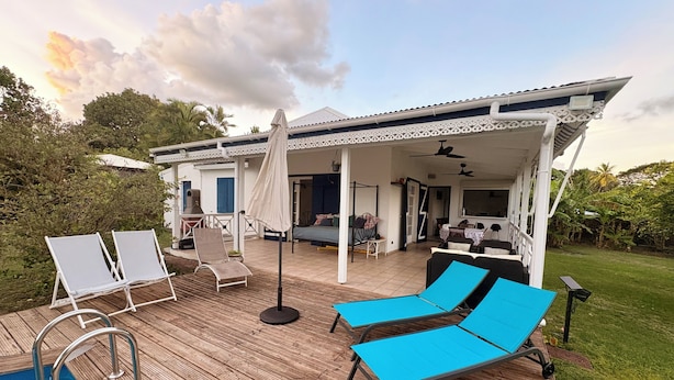 Uma área à beira da piscina com espreguiçadeiras, um terraço coberto e vista para a casa.
