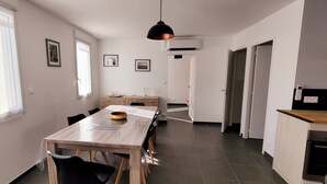 Moderni keittiö, jossa on puinen työtaso, ruokailutila puupöydällä ja -tuoleilla sekä käytävä, joka johtaa ovelle.