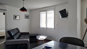 Moderni olohuone, jossa on sohva, ruokapöytä ja seinälle asennettu televisio.
