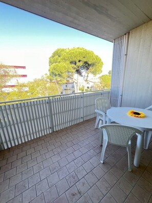 A balcony with a table and chairs, a view of trees, and a building in the background. - Flat Near the Beach With Terraces (San Michele al Tagliamento)