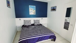 A bedroom with a bed, a nightstand, a wall-mounted light, and a door with a mirror. - Central house in quiet alley (La Tranche-sur-Mer)