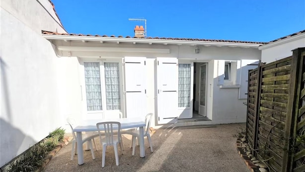 A white building with a tiled roof, a door, a window, a table with chairs, and a wooden fence. - Central house in quiet alley (La Tranche-sur-Mer)